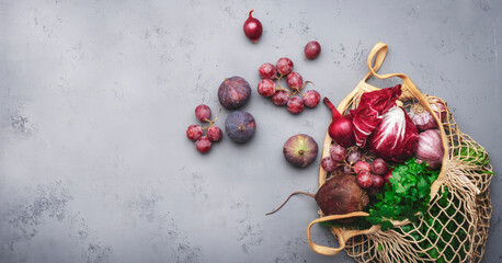 Autumn food background with purple vegetables, roots and fruits in string shopping bag: radicchio,...