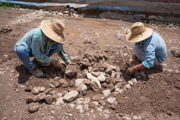 Dos obreros con sus manos están reparando y colocando las piedras en una calle de un pueblo.
 - obrazy, fototapety, plakaty