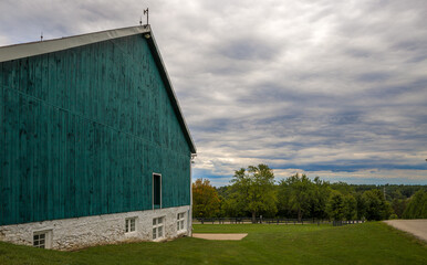 Fototapeta na wymiar Rural landscape - old farm, green barn, field and garden, cloudy sky