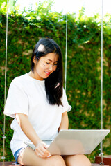 Cheerful young Asian woman smiling while working on her laptop outside the office, at home, working in the park. work holiday at home and working online