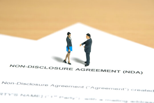 Miniature people toy figure photography. Nondisclosure contract agreement sign concept. A businesswoman walking above nondisclosure agreement file document
