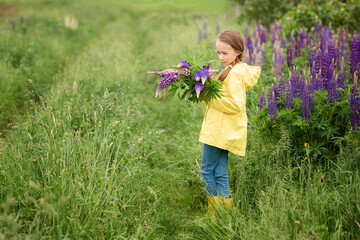 portrait of a cute little happy eight-year-old girl in a yellow jacket with blooming lupine flowers in a field of purple flowers. nature in the open air. The concept child in nature. Summer holidays