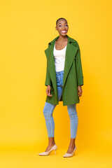 Fototapeta premium Full length portrait of trendy fashionable African American woman standing in yellow color studio isolated background