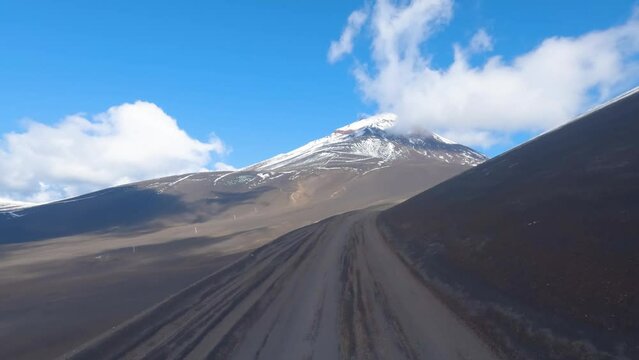 Viajando por un camino de tierra ripio con montañas nevadas, cielo azul y nubes. Imagen desde el techo de una camioneta con una camara de acción