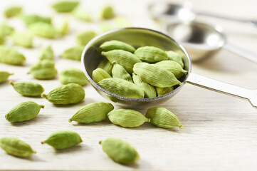 Cardamom pods in measuring spoons on white wooden kitchen table. Cooking concept.