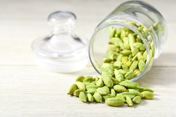 cardamom pods spill out of a glass storage jar on a  white wooden kitchen table, selective focus.