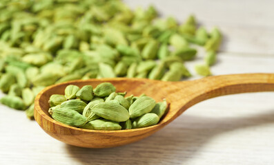 Cardamom pods in a wooden spoon on white wooden kitchen table, selective focus.