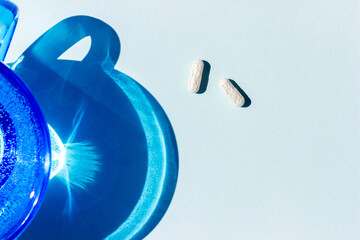 Two white pills and glass of water on blue background with copy space. Medicine, healthcare concept. Top view Flat lay