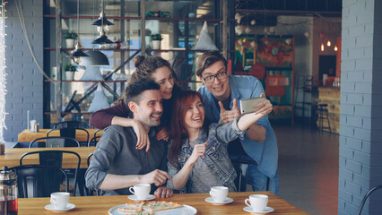 Cheerful young people popular bloggers are taking selfie posing laughing and having fun in cafe. Modern technology, social media, friendship and leisure time concept.