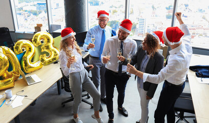 Business people are celebrating holiday in modern office drinking champagne and having fun in coworking. Merry Christmas and Happy New Year 2023.