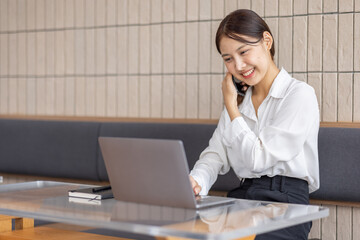 Asian businesswoman talking on phone, using laptop, looking at screen, entrepreneur manager consulting client by call, looking at computer screen, discussing project, reading information