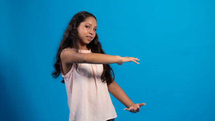 Niña con blusa rosa con fondo azul usando, señalando con sus dedos.