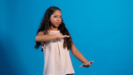 Niña con blusa rosa con fondo azul usando, señalando con sus dedos.