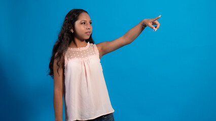 Niña con blusa rosa con fondo azul usando, señalando con sus dedos.