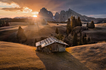 Alpe di Siusi, Italy - Beautiful autumn sunrise with a wooden chalet at Seiser Alm, a Dolomite plateau in South Tyrol province in the Dolomites mountain range with colorful golden sky