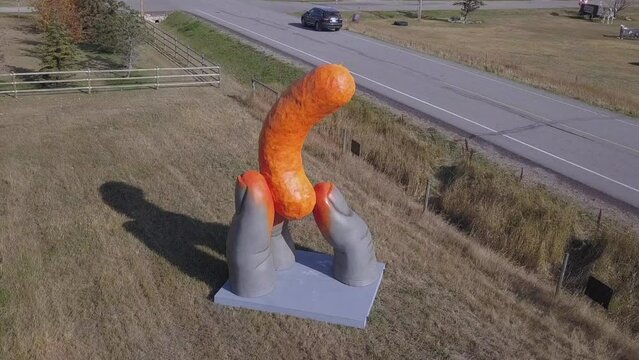 Amusing orange statue of Cheadle Cheeto snack held by three fingers
