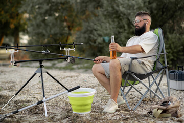 happy man fishing and drinking beer on shore of sea or lake, handsome man relaxing with beer...