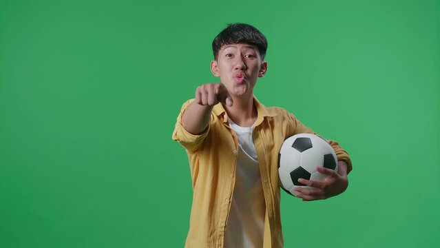 Asian Boy With A Ball Pointing To Camera For Making Fun Of The Losers While Cheering Soccer On Green Screen Background
