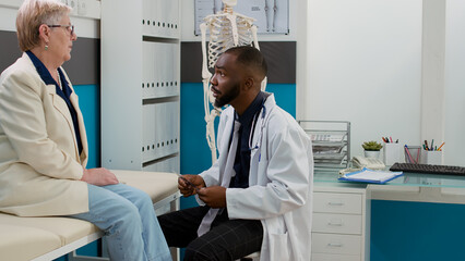 General practitioner looking at bones x ray with senior patient, analyzing radiography scan diagnosis to give healthcare treatment and support. Male doctor and old woman talking about disease.