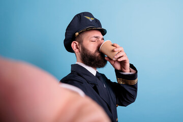 Pilot drinking coffee to go first person view, taking selfie on front camera, fpv. Middle aged airlane captain in uniform holding take away tea paper cup pox, making photo on mobile phone