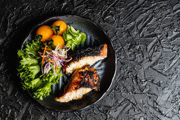 Grilled tilefish marinated with saikyo-miso and tomato salad on a black plate against a black design board.