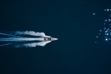 super fast open big boat with people moving fast on dark blue water making a white trail behind the...