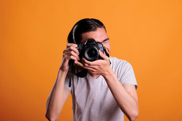 Photographer taking photos on professional dslr camera, young asian man photographing, front view medium shot. Teenager looking in device viewfinder, creative hobby, photoshoot