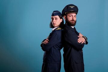 Airplane captain and flight attendant in professional airline uniform standing back to back portrait, studio medium shot. Airliner crew, plane aviator and stewardess, team side view