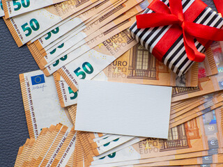 Fototapeta premium Blank sheet with copy space on the background of fifty euros banknotes with gift box. Set of European Union money. Enterprise capital investment, finance, savings, buying gifts, spending money concept