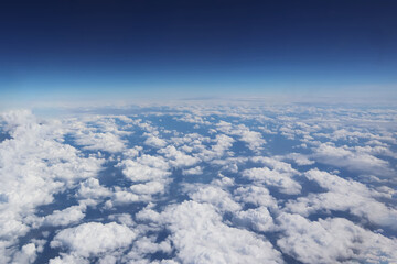 Aerial view from aircraft above soft white clouds with horizon freshness and peaceful deep blue sky for meteorology presentation background.