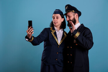 Smiling pilot using and flight attendant talking on smartphone videocall together. Airlane captain...