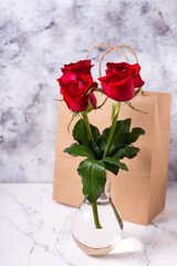 Postcard with red colorful summer roses  flowers and  paper bag with  present against grey textured background  Selective focus. Still life. Place for text.