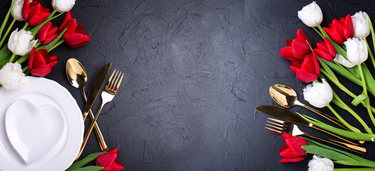 Romantic background postcard.White and red tulips flowers, plates on black textured background. Place for text.