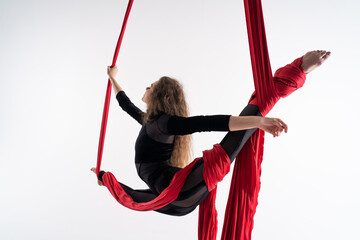 Flexible female circus Artist perform on red aerial silk on white background