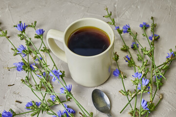 chicory drink in a coffee mug and a spoon next to chicory flowers