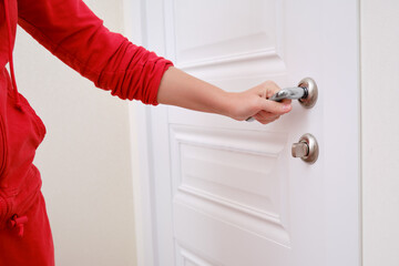 A woman opens the door holding the handle, hand close-up. White wooden door, metal door handle and female hand