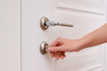 A woman opens the door holding the lock, hand close-up. White wooden door, metal door handle and female hand