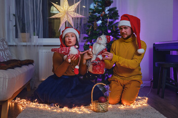 An adult man and a woman play a homemade puppet show at the Christmas tree. Home family leisure with a Christmas story on New Year Eve in the evening living room