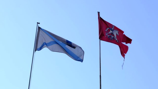St. Andrew's flag and flag of city of Moscow develop against background of sky. Close-up