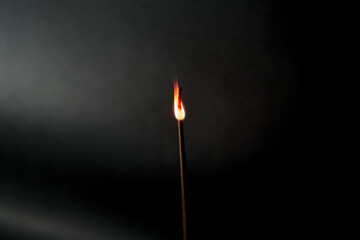 Close-up of glowing incense stick with flame against black background with spotlight. Photo taken...