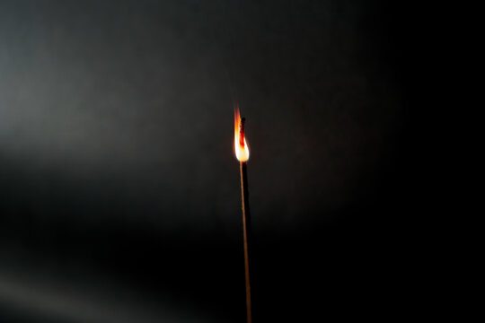 Close-up of glowing incense stick with flame against black background with spotlight. Photo taken October 9th, 2022, Zurich, Switzerland.