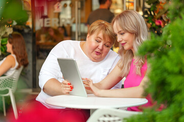 Mother with disability in wheelchair and her daughter using digital tablet while sitting at the table in cafe