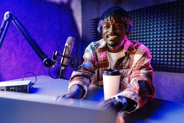 African radio host sitting at desk recording in studio with microphone and laptop