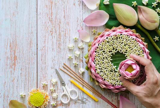 Pink lotus petal krathong for Thailand Loy Krathong festival decorates from lotus, crown flower, incense stick and candle with blurred focus of hand holding lotus flower on wooden background.
