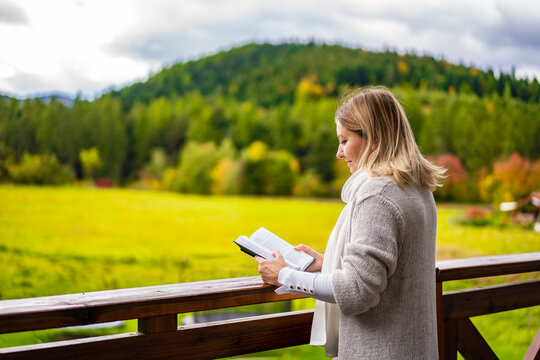 Beautiful woman standing on terrace reading book  contemplating nature