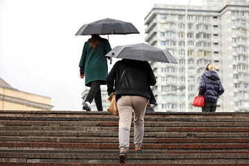 People with umbrellas walking up the steps on city buildings background. Rain in autumn city