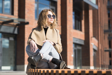 Portrait of a young Caucasian girl in a coat who is sitting on a bench.