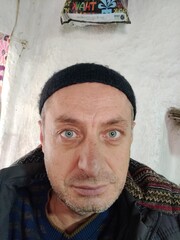 A man in a headscarf, a metaphor for resilience, gazes with quiet strength against a rustic wall,...