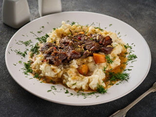 Beef cheeks with mashed potatoes on white plate.