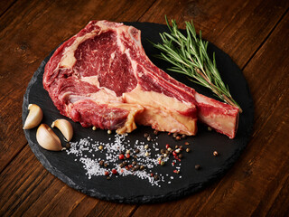 Raw tomahawk beef steak with ingredients for grilling, rosemary, salt, pepper and garlic.